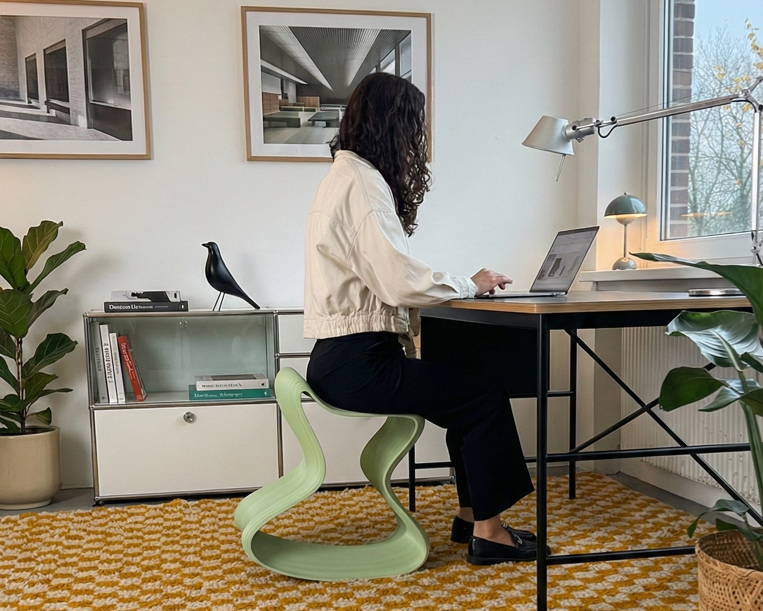 Person working in a modern home office on a mint green Flow Chair. An ergonomic stool styled with USM Haller sideboard and Vitra accessories. Best homeoffice furniture 2026 candidate by boldobjects.